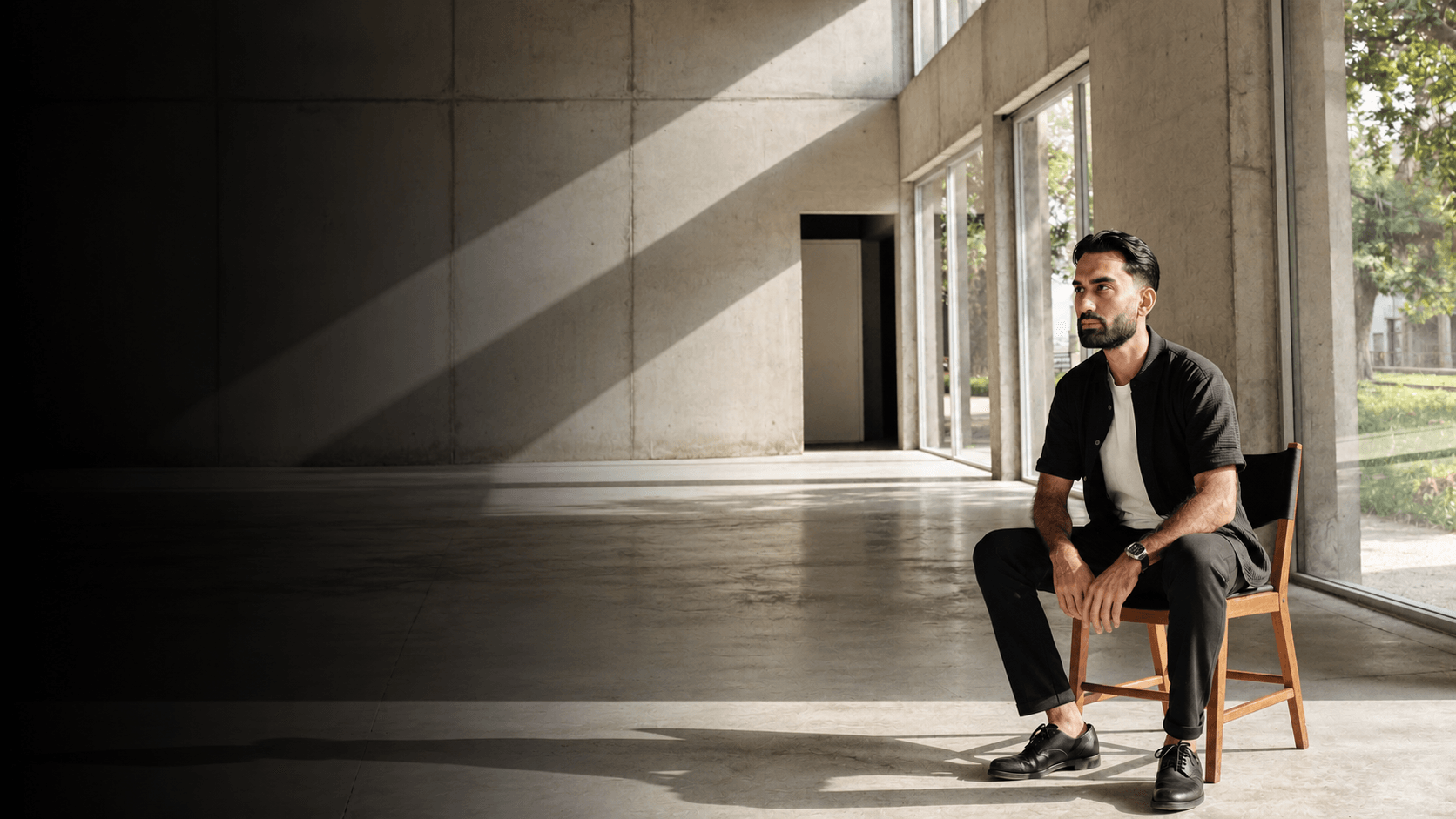 Jay Chaudhry seated on a wooden chair in a sunlit concrete room