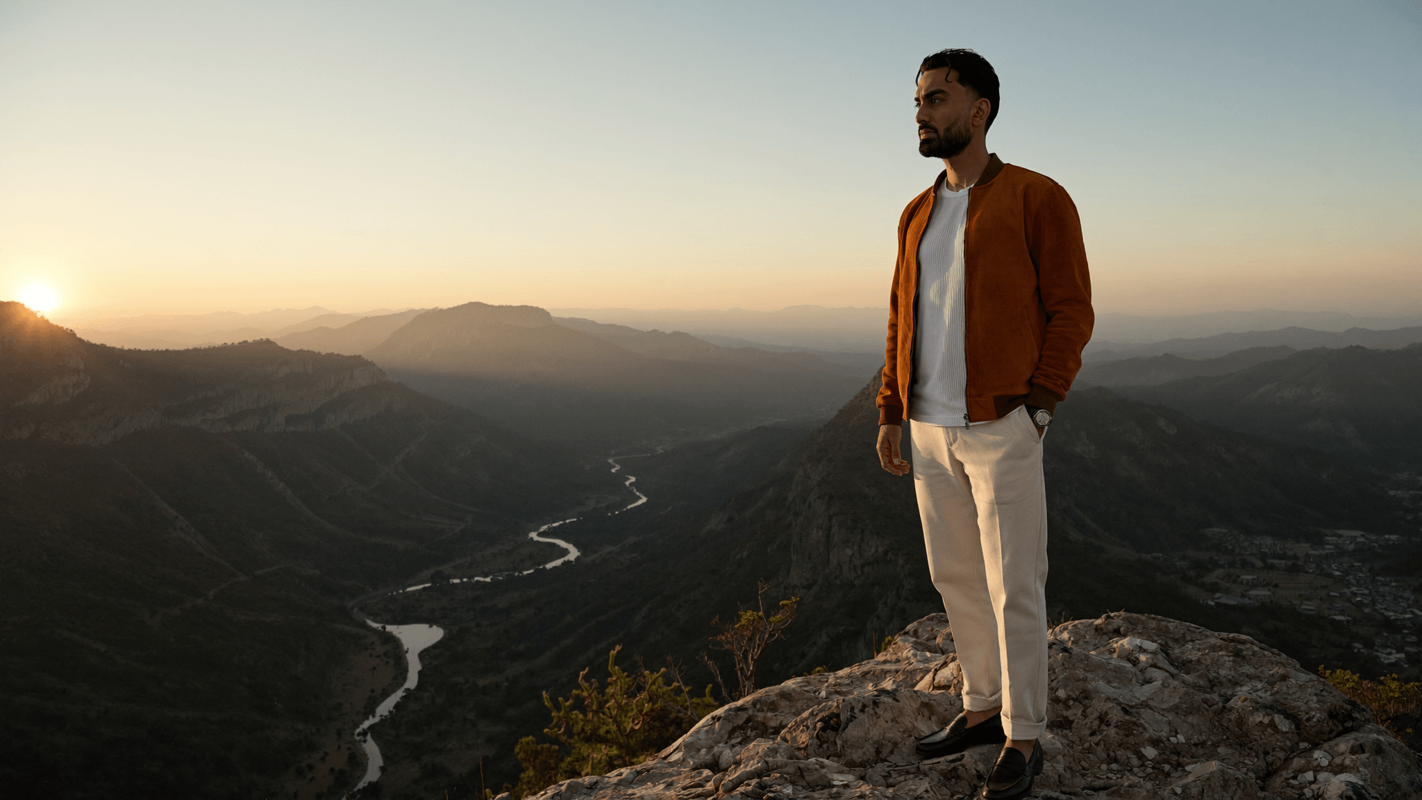 Jay Chaudhry standing on a mountain ridge at sunset above a river valley